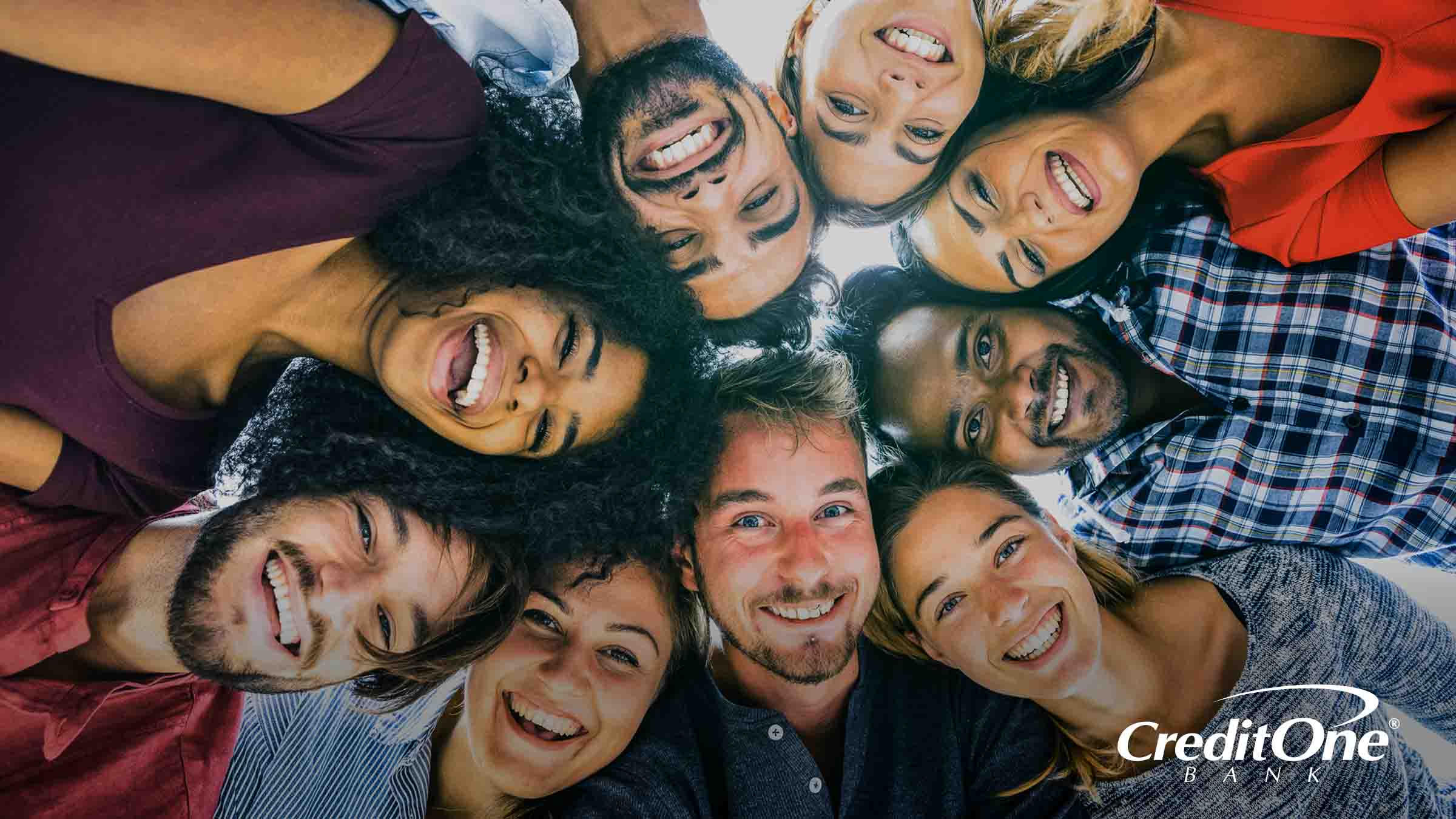 A diverse friend group of millennials gathers in a huddle, smiling happily while considering how credit scores affect their social status.