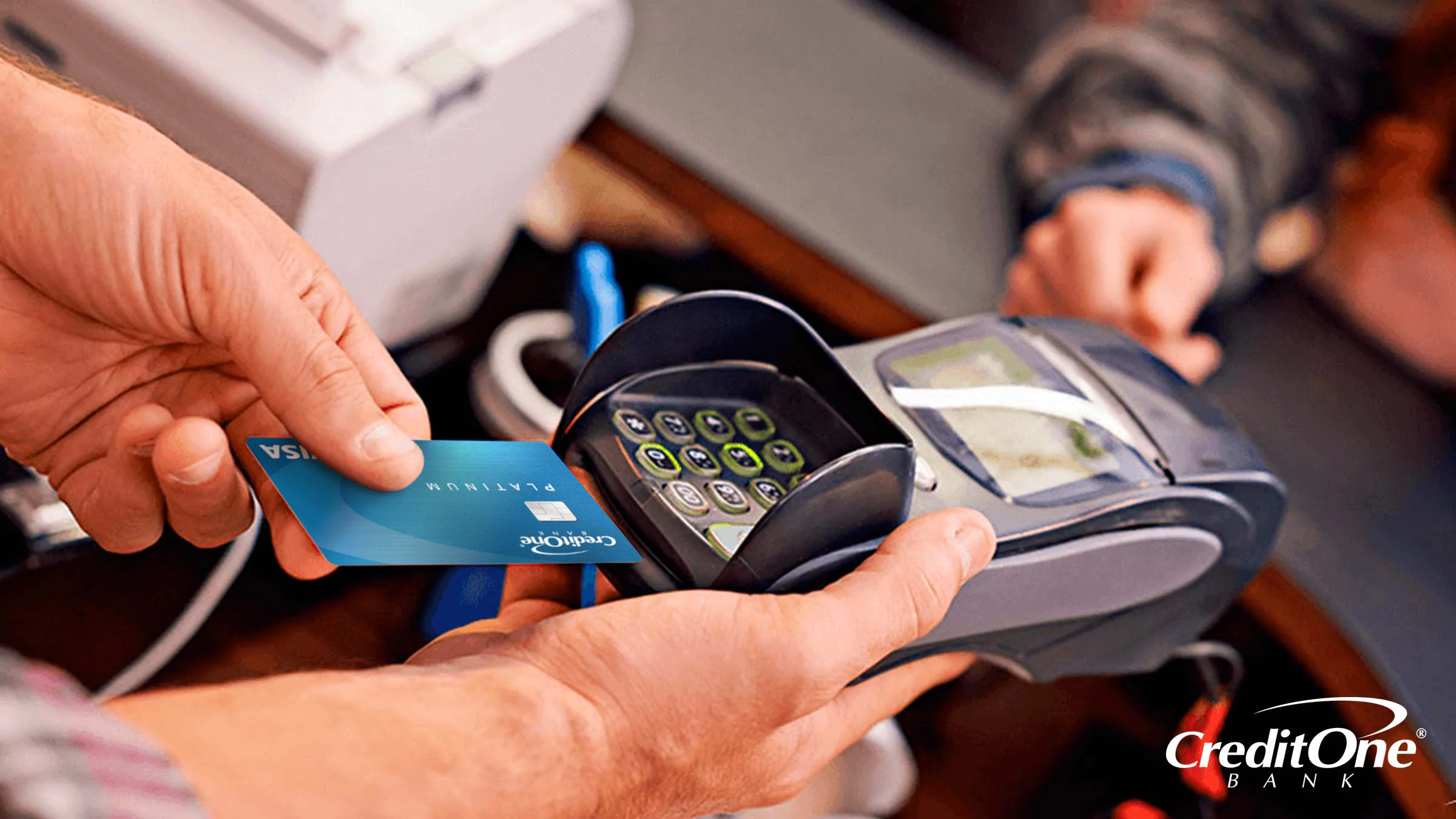 A man’s hands hold a portable credit card reader at a checkout counter while preparing to insert a credit card with an EMV chip.