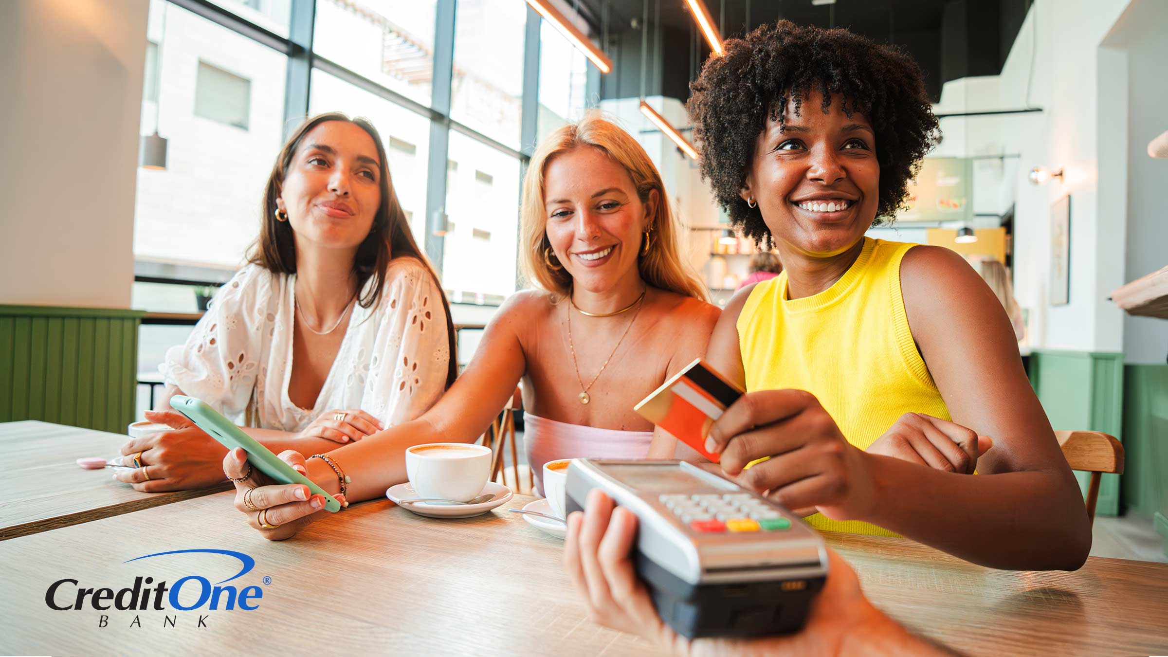 Three happy women are at a restaurant as one pays the bill with what could be a dining rewards card, which could be one of multiple credit cards she has for different situations.