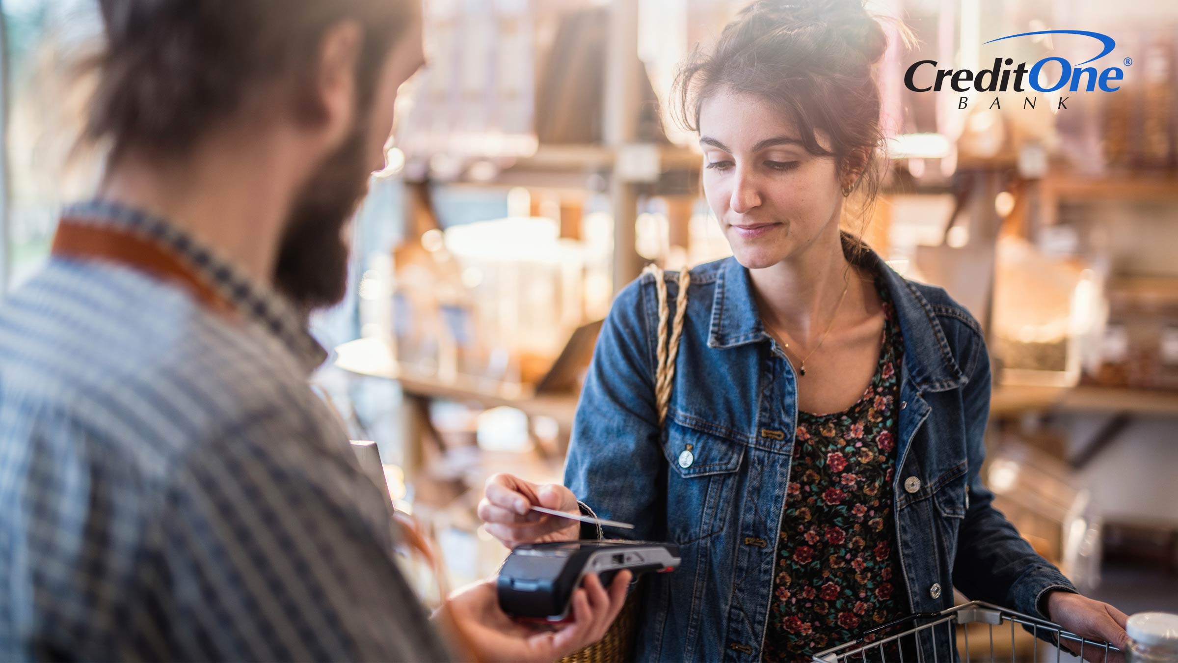A woman taps her card to pay on a male clerk’s handheld terminal in a small shop. She may prefer credit versus cash for purchases.