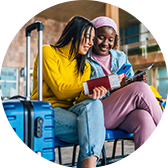 Two women looking at a smartphone while seated with luggage and airline tickets