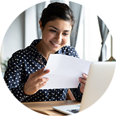 A woman looking at a document, seated in front of a laptop