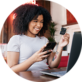 A young consumer smiling and looking at her credit card, while sitting in front of her laptop