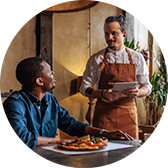 A man seated at a restaurant, talking to the wait staff